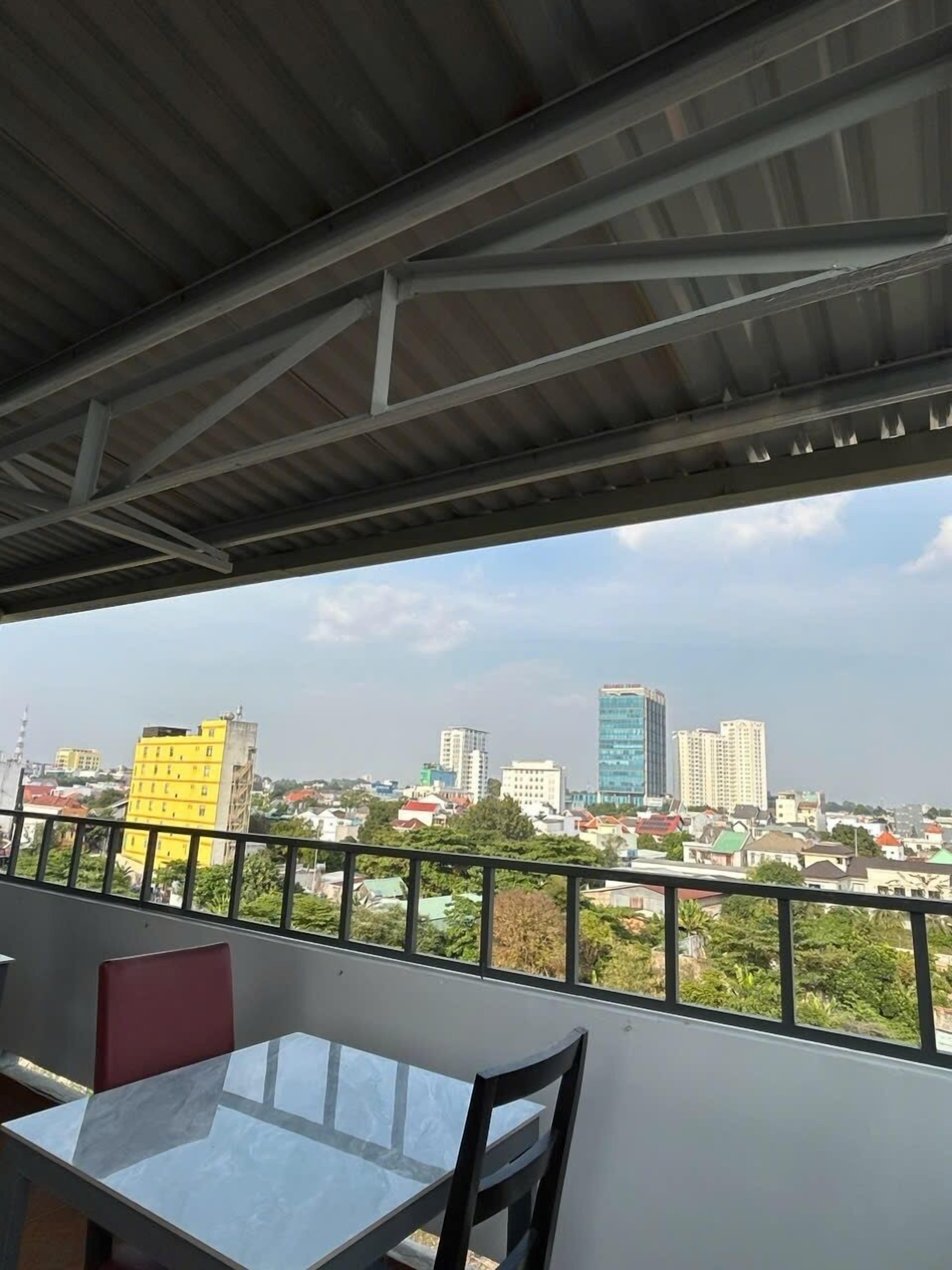 A balcony with a table and chairs, overlooking a cityscape with various buildings.
