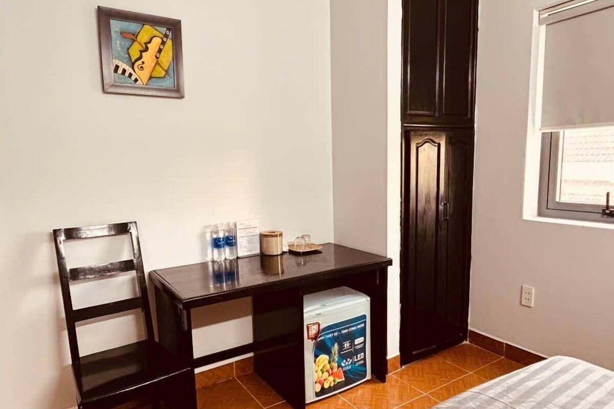 Quarto pequeno com cama, escrivaninha, cadeira, guarda-roupa e janela.