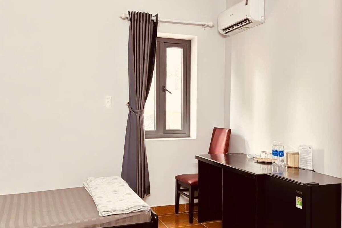 Quarto pequeno e limpo, com duas camas, uma escrivaninha, uma cadeira e ar condicionado.