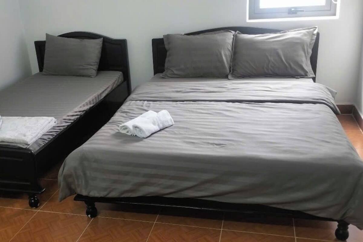 Quarto com duas camas, cada uma com roupa de cama e almofadas cinzas, e uma pequena mesa com uma toalha dobrada.