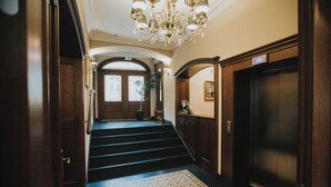 A grand staircase with a patterned carpet leading to a door with a sign indicating the elevator. - HG Hotel Restauracja (Toszek)