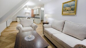 A living room with a wooden coffee table, two white sofas, a painting on the wall, and a kitchen in the background. - HG Hotel Restauracja (Toszek)