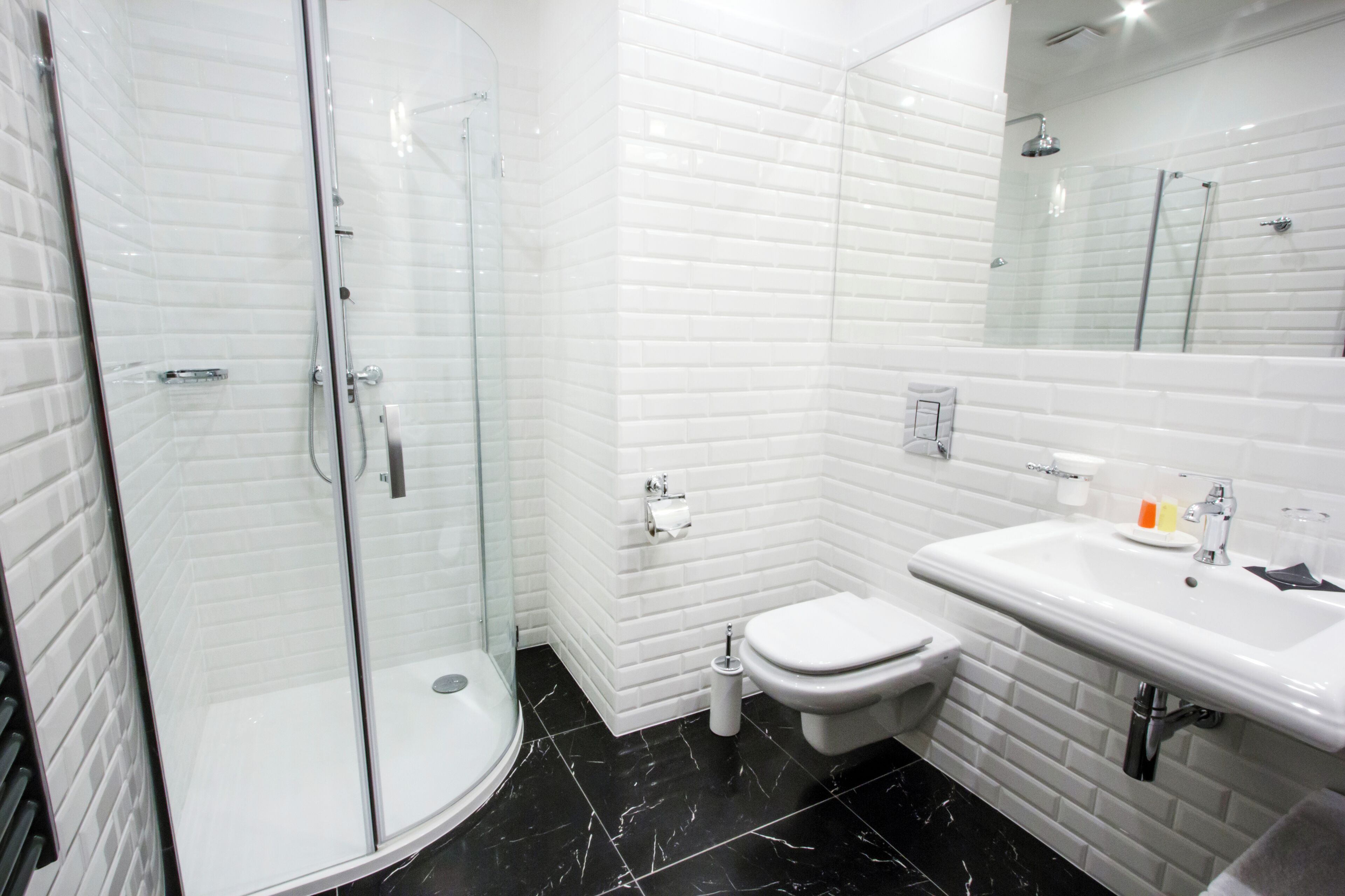 Une salle de bain moderne avec une douche à parois de verre, des toilettes blanches et un lavabo surmonté d’un miroir.
