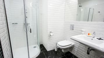 Un baño moderno con ducha envuelta en vidrio, inodoro blanco y lavamanos con espejo arriba.