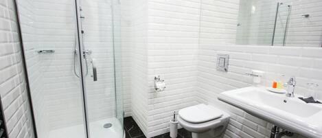 Une salle de bain moderne avec une douche à parois de verre, des toilettes blanches et un lavabo surmonté d’un miroir.