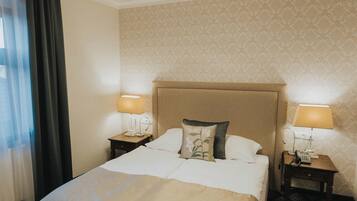 Une chambre d’hôtel avec un grand lit, deux tables de chevet avec des lampes, une bouche d’aération au plafond et une moquette à motifs.