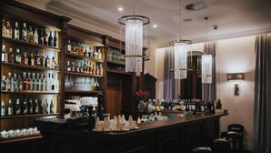 A bar area with shelves of liquor bottles, a bar counter with glasses and bottles, and two hanging crystal chandeliers. - HG Hotel Restauracja (Toszek)