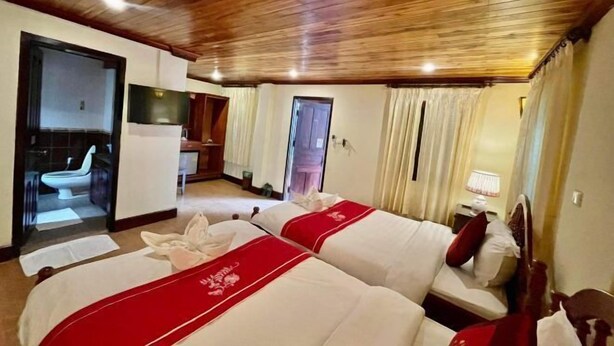 A hotel room with two beds, wooden ceiling, a television, and a bathroom visible through an open door.