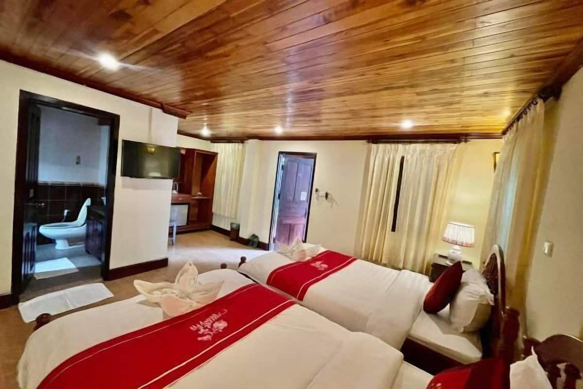 A hotel room with two beds, wooden ceiling, a television, and a bathroom visible through an open door.