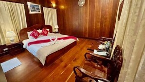 A wooden-paneled room with a bed, a desk, a chair, a fan, and curtains.