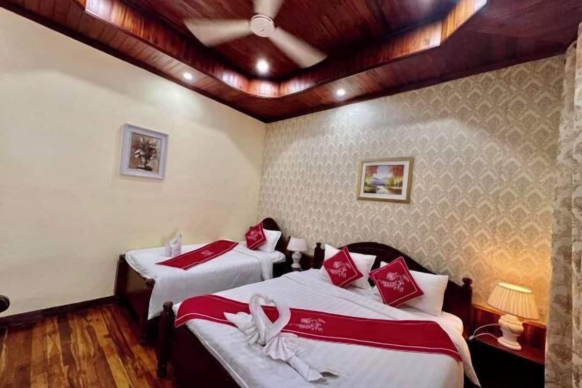 A hotel room with two beds, wooden ceiling, patterned wallpaper, and a ceiling fan.