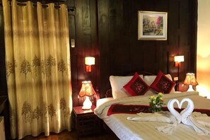 Una habitación de hotel con cama, cortinas, lámparas y un cuadro en la pared.