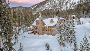 Ein großes, mehrstöckiges Holzhaus mit einem Steinkamin, umgeben von schneebedeckten Bäumen und einer bergigen Landschaft.