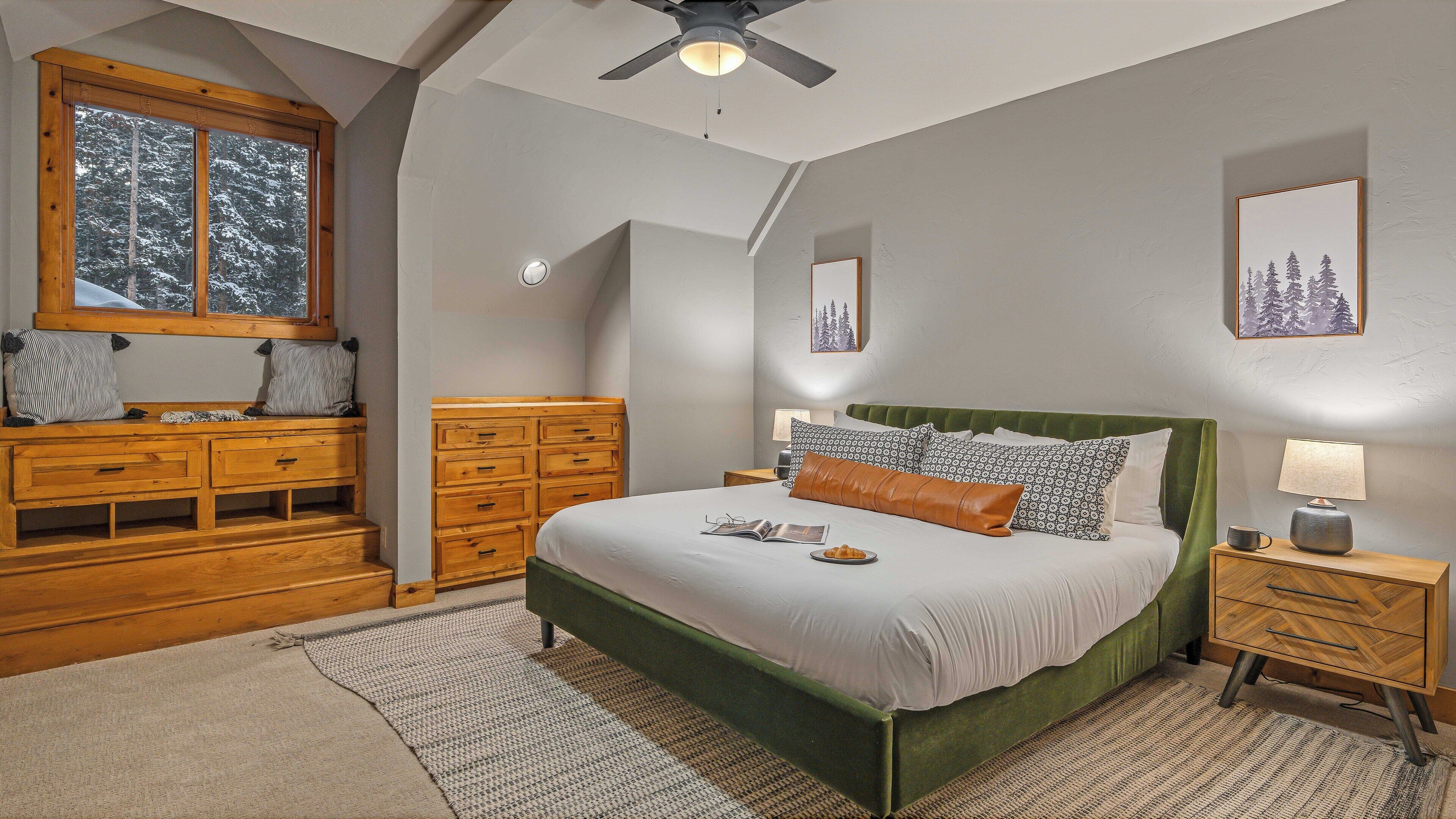 Quarto com cama, cómoda de madeira, mesa de cabeceira e janela com vista para árvores cobertas de neve.