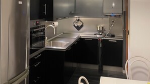 A compact kitchen with a refrigerator, oven, and sink. There is a dining table with chairs and a pendant light above. - Lofts with breathtaking views (Gorizia)