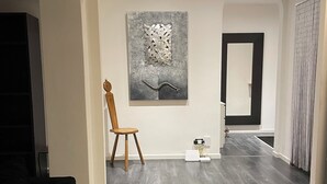 A modern living room with dark wooden flooring, a wooden chair, a large abstract painting on the wall, and a black-framed mirror. - Lofts with breathtaking views (Gorizia)