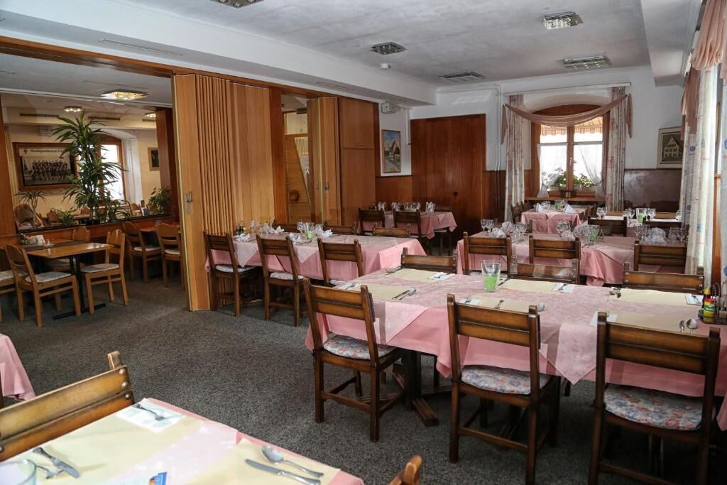 Ein Essbereich mit mehreren Tischen, die mit rosa Tischdecken bedeckt sind, Holzstühlen und einer großen Pflanze im Hintergrund.