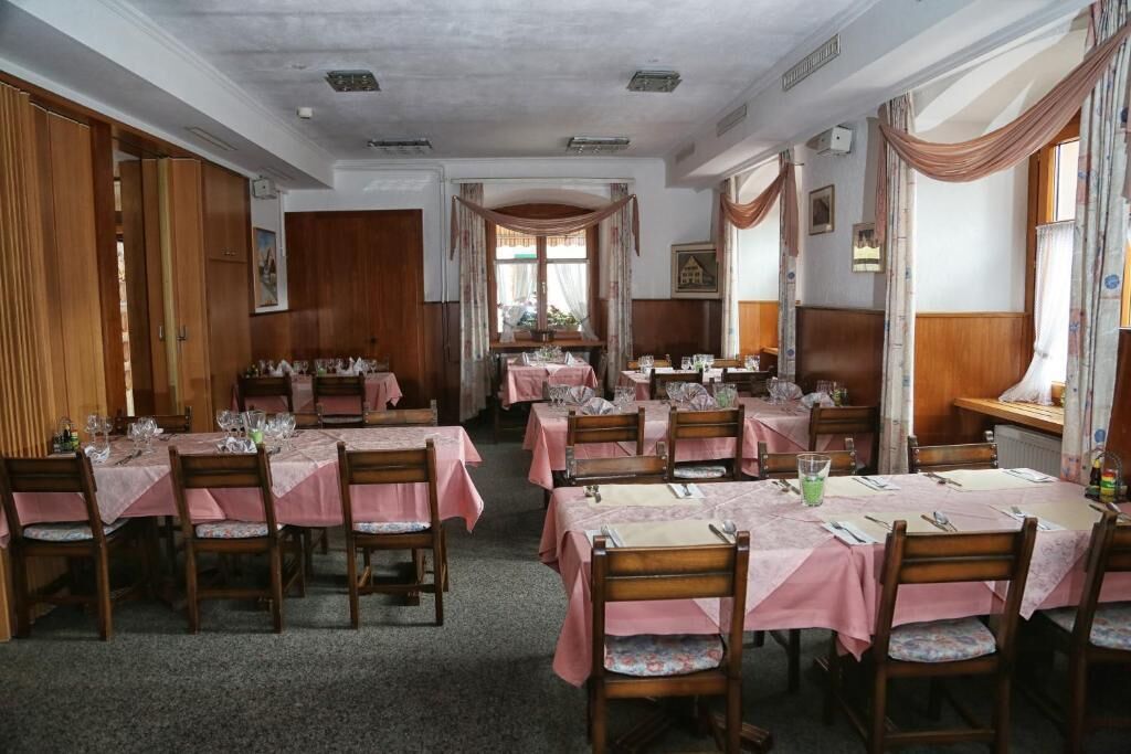 A dining area with multiple tables set for a meal, featuring wooden chairs and pink tablecloths.