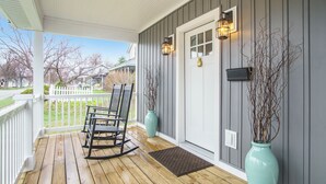 A wooden porch with rocking chairs, a mailbox, and a door with a light fixture. - Fabulous, 4 Bedroom, 3 Bathroom home in Downtown Ludington (Ludington)