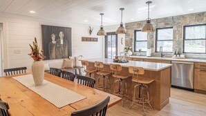 Una cocina moderna con una isla de madera, taburetes de bar, luces colgantes y salpicadero de piedra.
