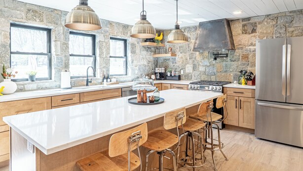Una cocina moderna con una isla grande, taburetes de madera, paredes de piedra y electrodomésticos de acero inoxidable.