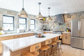 A modern kitchen with a large island, wooden bar stools, stone walls, and stainless steel appliances.