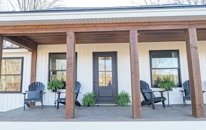 A covered porch with wooden beams, black chairs, and potted plants.