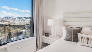 Een hotelkamer met een groot raam, een bed, een nachtkastje en een lamp.