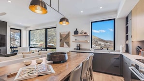 Een moderne keuken met een houten eettafel, inbouwapparatuur en grote ramen met uitzicht op de bergen.