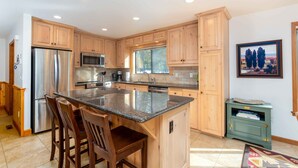 A modern kitchen with wooden cabinets, stainless steel appliances, and a large island with bar stools. - JACK01 - Family Friendly Sunriver Getaway (Sunriver)