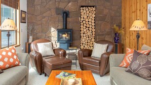 A cozy living room with leather sofas, a coffee table, and a stone fireplace with a wood log display. - JACK01 - Family Friendly Sunriver Getaway (Sunriver)