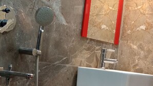A bathroom with a marble wall, a shower, a sink, and a red-framed mirror. - Asha Inn (Barasat)