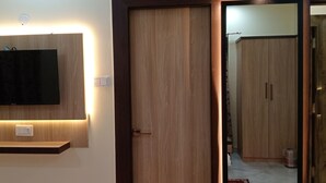 A room with a wooden door, a wall-mounted shelf, and a flat-screen TV. - Asha Inn (Barasat)