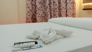 A neatly made bed with a white blanket, a remote control, and a pair of slippers. - Asha Inn (Barasat)