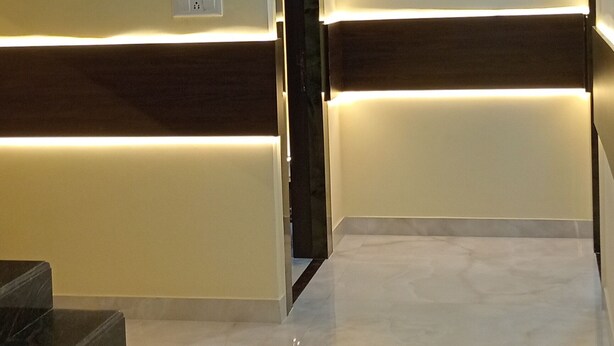 A hotel lobby with a marble staircase, a reception desk with a lighted wall, and a ceiling with recessed lighting. - Asha Inn (Barasat)