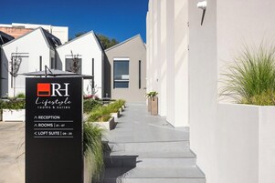 Une entrée d’hôtel moderne avec un comptoir d’accueil, un escalier et un chemin menant au bâtiment.