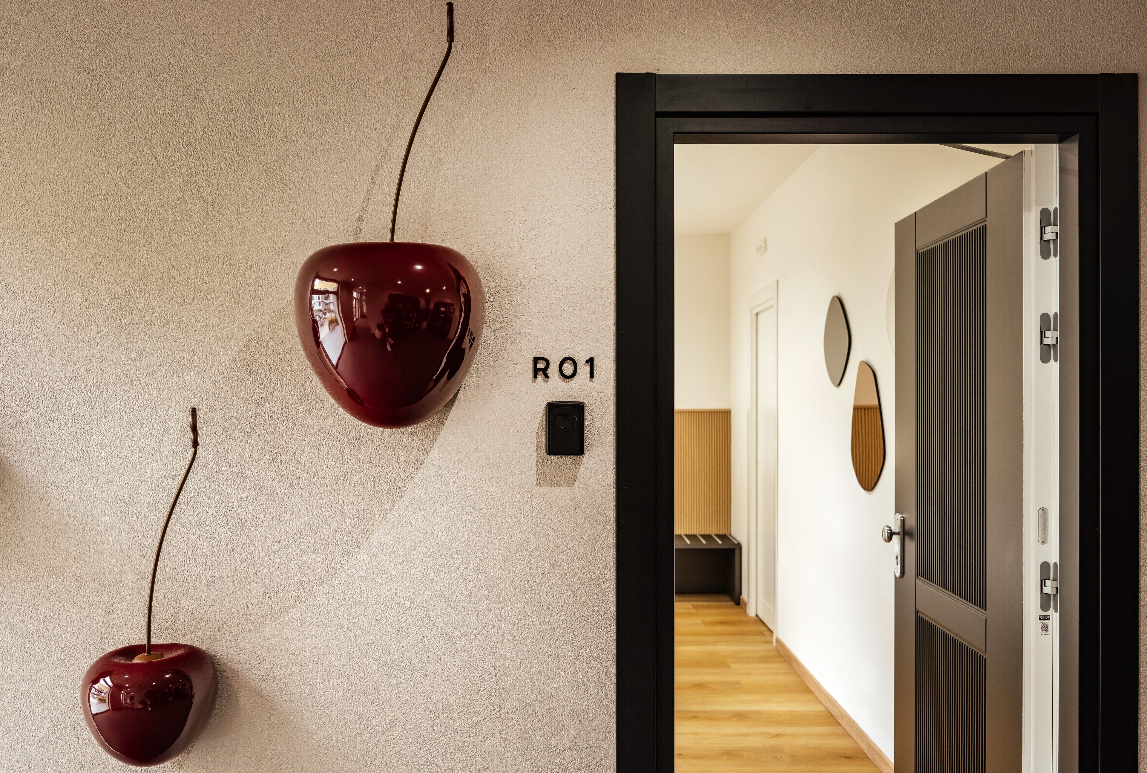 A hallway with a wall-mounted red object, a door labeled "R01", and a wooden floor.