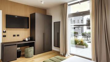 Ein modernes Hotelzimmer mit großem Fenster, einem an der Wand befestigten Flachbildfernseher, einem Schreibtisch mit Stuhl und einem Kleiderschrank.