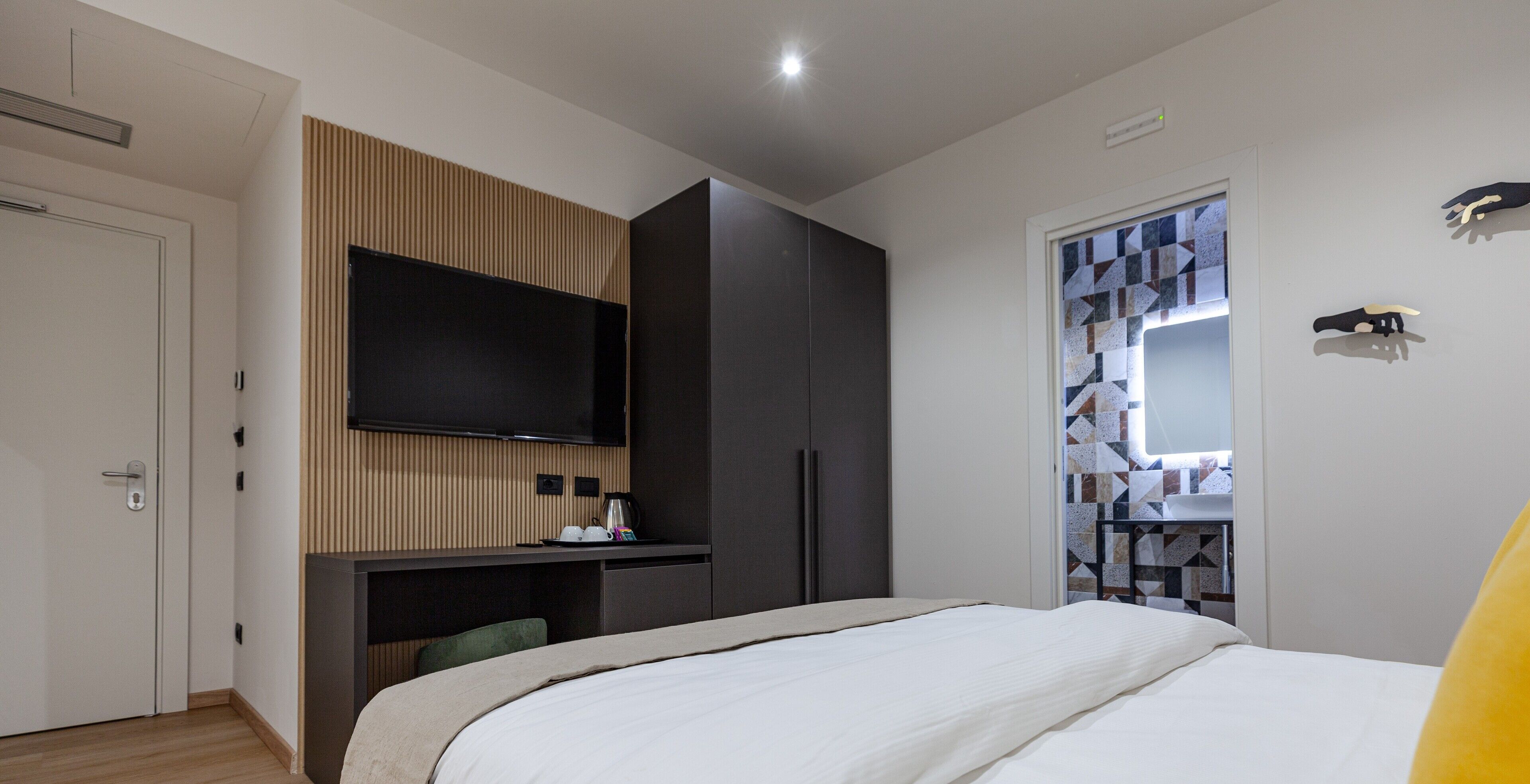Una habitación de hotel moderna con una cama, un televisor montado en la pared, un escritorio con silla y un armario.