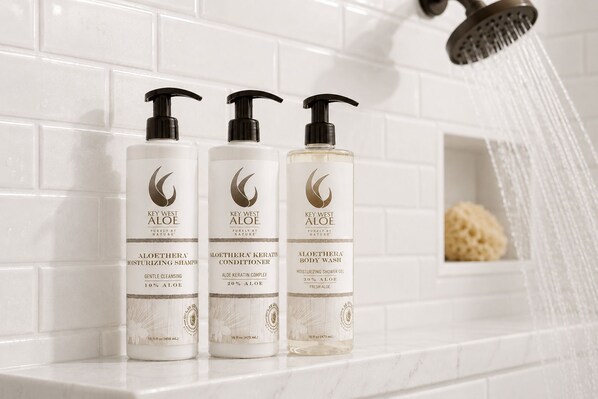 Tres botellas de productos Key West Aloe sobre una encimera de baño con una alcachofa de ducha.