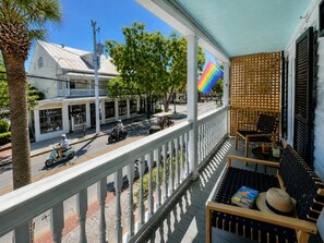 Un balcon donnant sur une rue, une clôture en bois et une table avec un livre et un chapeau.