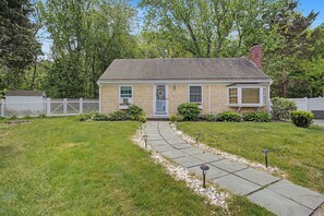 A single-story house with a front yard, a pathway leading to the front door, and a white picket fence.