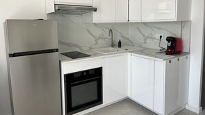 Eine moderne Küche mit weißen Schränken, einem Edelstahl-Kühlschrank, einem Einbauofen, einer Marmor-Spritzschutzwand und einer Kaffeemaschine auf der Arbeitsplatte.