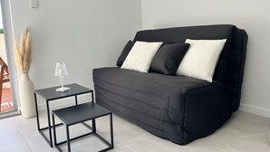Ein modernes Wohnzimmer mit einem schwarzen Sofa, zwei weißen Kissen, einem kleinen schwarzen Beistelltisch und einer klaren Glasvase mit Pampasgras.
