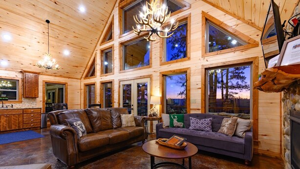 A spacious log cabin interior with a leather sofa, a smaller couch, and a round coffee table. - 8 BR sleeps 29 river front *private island* pool tables (Smithville)