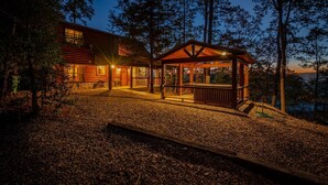 A cabin with a wooden exterior, a covered porch, and a view of the surrounding forest. - 8 BR sleeps 29 river front *private island* pool tables (Smithville)