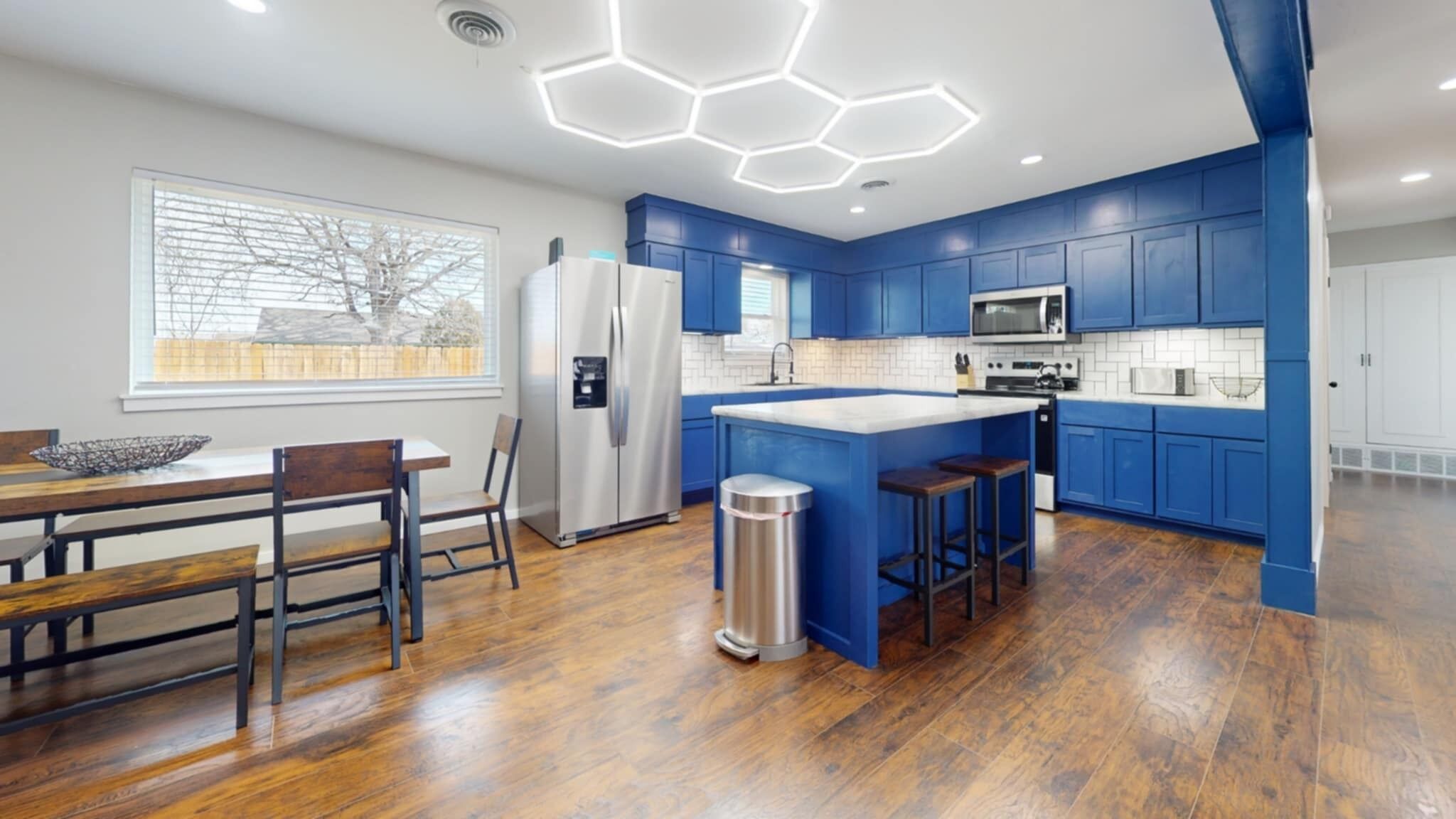 A modern kitchen with blue cabinets, a stainless steel refrigerator, a microwave, and a large island with stools.