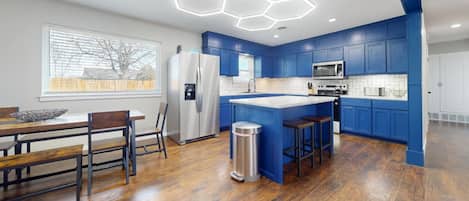 A modern kitchen with blue cabinets, a stainless steel refrigerator, a microwave, and a large island with stools.