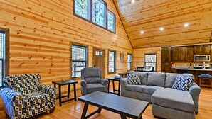 A spacious log cabin interior with a large living area, wooden walls, and a kitchen area.