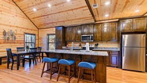 A wooden cabin interior with a kitchen area featuring a central island, bar stools, and a refrigerator.